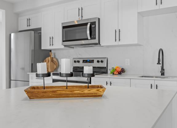 A modern kitchen with a white countertop and a wooden cutting board on it.