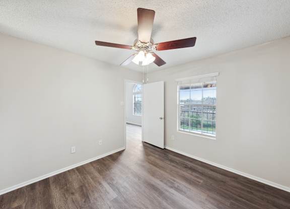 A room with a ceiling fan and a window overlooking a balcony.