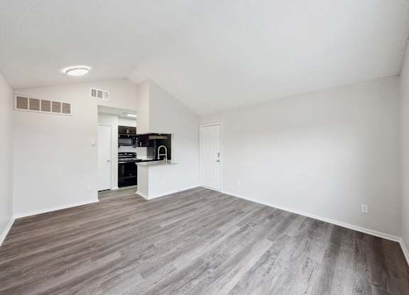 A room with a wooden floor and a kitchen area in the background.