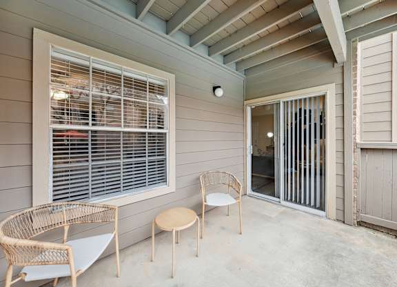 A patio with a table, chairs, and a sliding glass door.