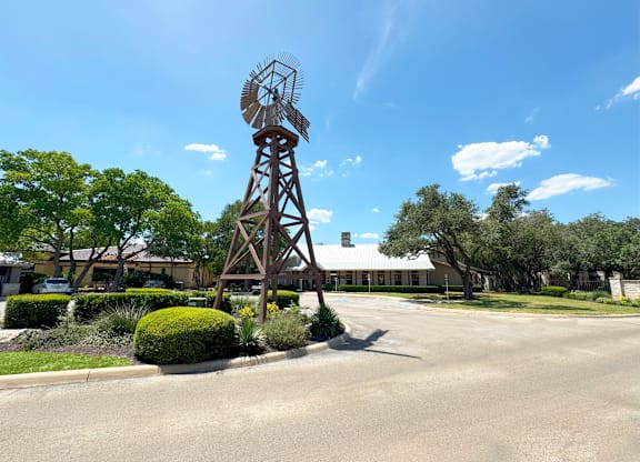 A windmill stands in the middle of a road with trees and bushes around it.