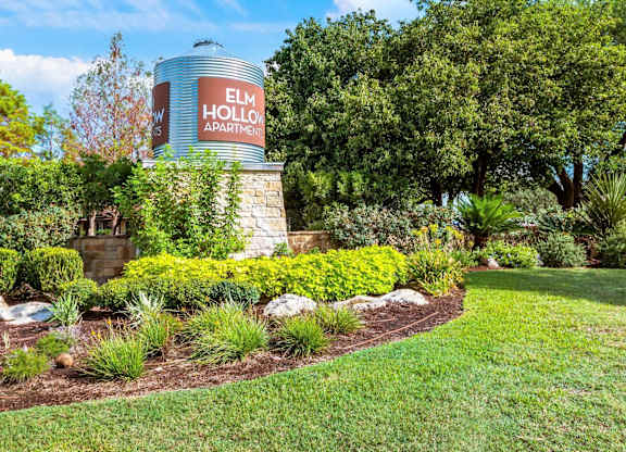 A sign for Elm Hollow Apartments is displayed on a water tower in a landscaped area.