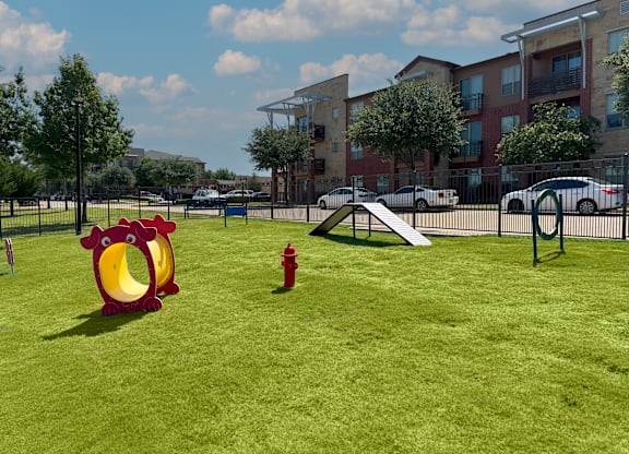 A playground with a red chicken slide and a red fire hydrant in a grassy area.