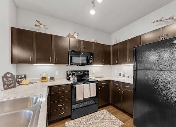 A kitchen with a black refrigerator and wooden cabinets.