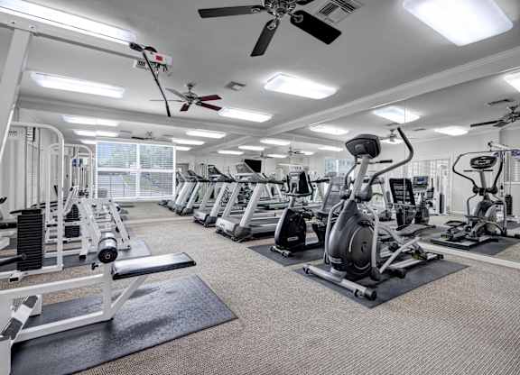 A spacious gym with a variety of equipment and a ceiling fan.