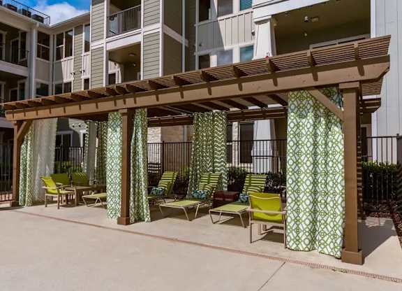 A patio with a wooden pergola and green chairs.
