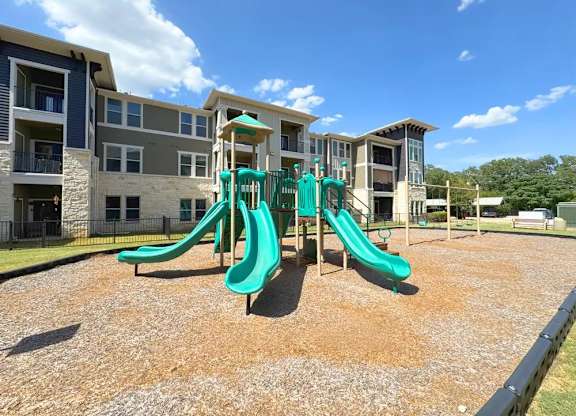 A playground with a green slide in front of apartment buildings.