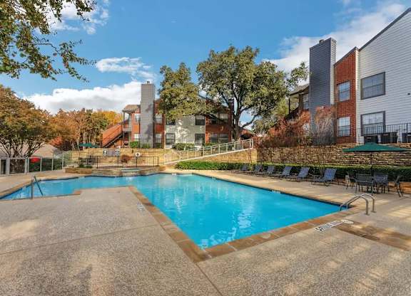 A swimming pool surrounded by a concrete deck and lounge chairs.