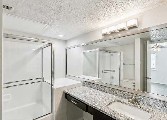 A bathroom with a white shower, sink, and mirror.
