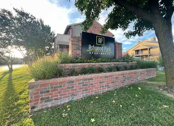 A sign for Ashwood Park Apartments is displayed in front of a brick wall.