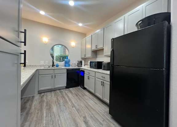 A black refrigerator is in a kitchen with white cabinets.