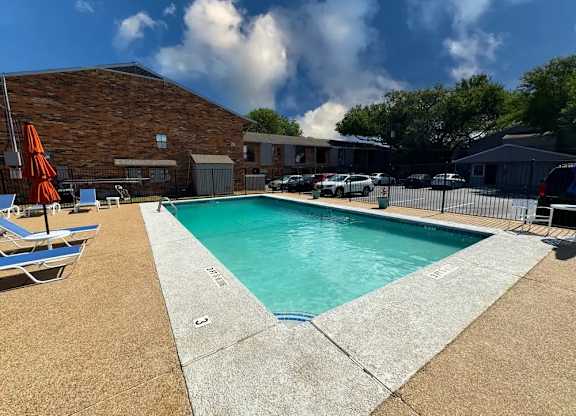 A pool surrounded by a concrete edge and a brick building.