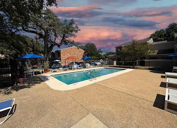 A pool surrounded by chairs and trees with a building in the background.