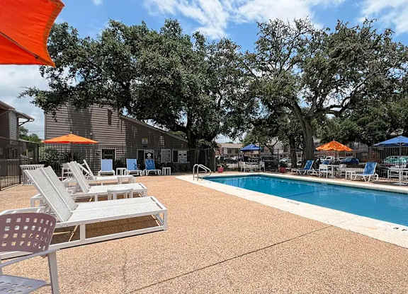 A pool surrounded by chairs and trees.