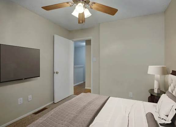 A bedroom with a bed, a ceiling fan, and a lamp.