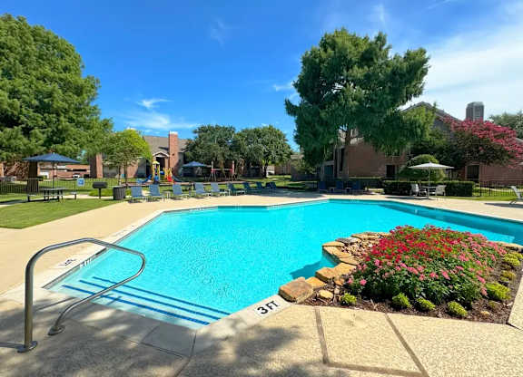 A pool surrounded by a flower bed and trees.
