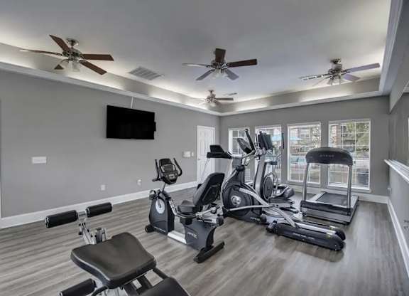 A spacious home gym with a variety of exercise equipment and a flat-screen TV mounted on the wall.