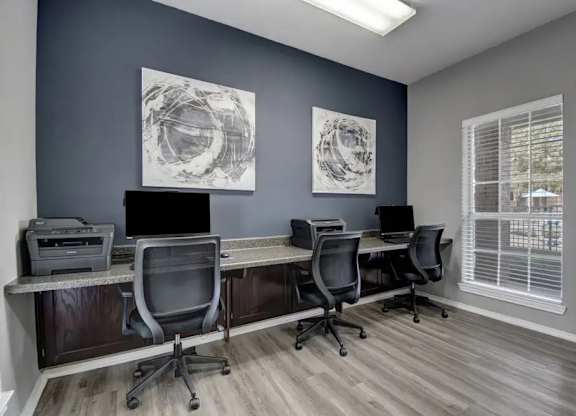 A room with a desk and chairs and two artworks on the wall.