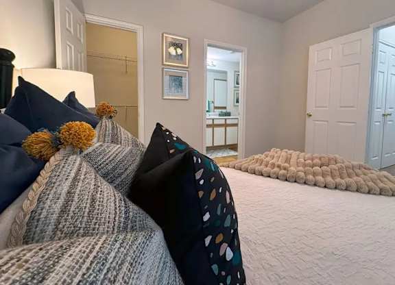 A bedroom with a bed covered in pillows and a rug on the floor.
