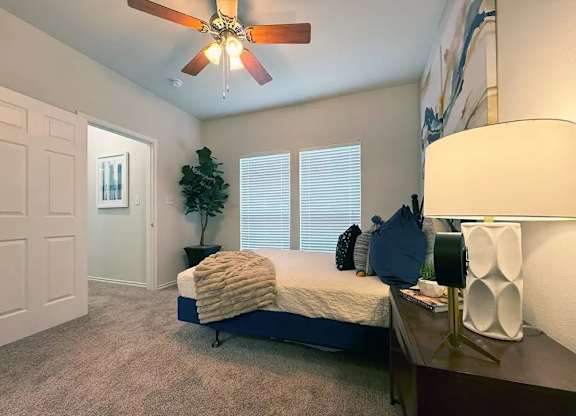 A bedroom with a bed, a ceiling fan, and a lamp.