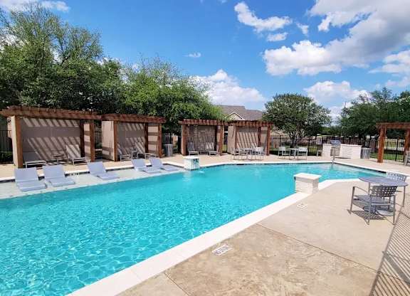 A large swimming pool surrounded by lounge chairs and wooden pergolas.