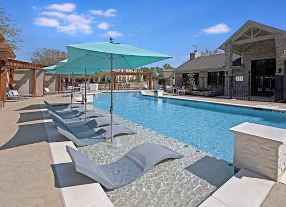 A pool with a blue umbrella and lounge chairs.