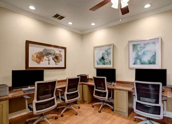 A room with a desk and chairs and two framed pictures on the wall.