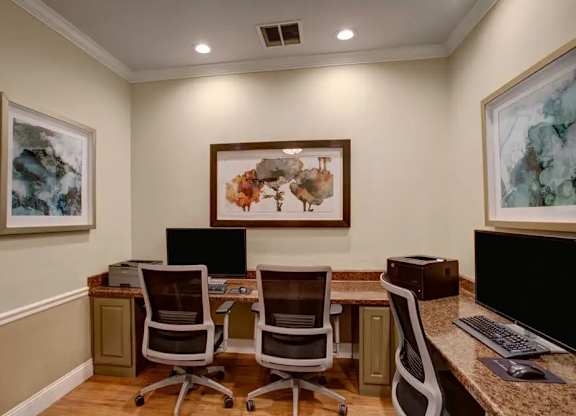 A room with a desk, chairs, and two framed pictures on the wall.