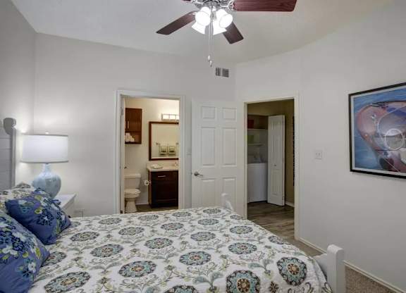 A bedroom with a patterned bedspread and a ceiling fan.