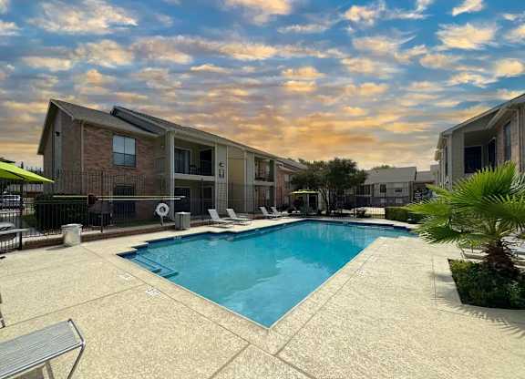 A swimming pool surrounded by a concrete patio and a building in the background.