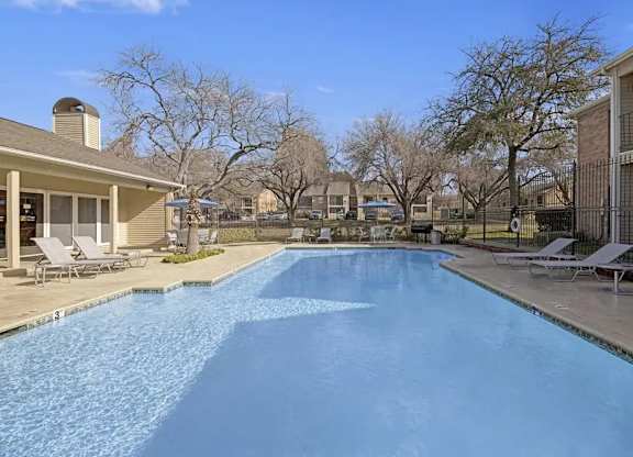 A swimming pool in a residential area with a house and trees in the background.
