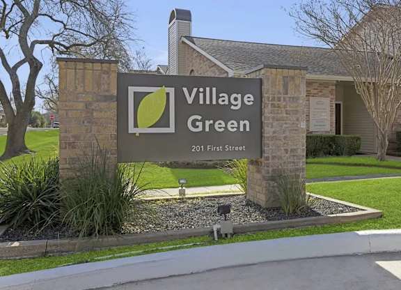 A sign for Village Green with a green leaf logo on it.