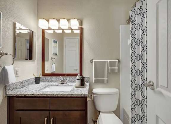 A bathroom with a toilet, sink, mirror, and a shower curtain.
