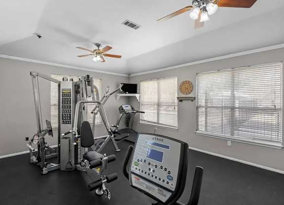 A home gym with a variety of exercise equipment and a ceiling fan.