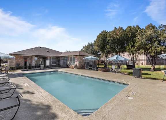 A swimming pool surrounded by lounge chairs and umbrellas in a sunny outdoor setting.