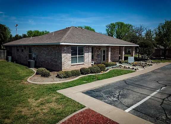 A small building with a grey roof and a parking lot in front.