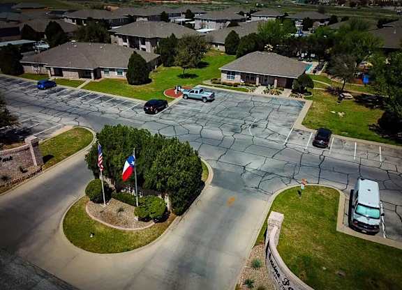 A residential street with cars parked on the side and a flagpole with the American and Texas flags.