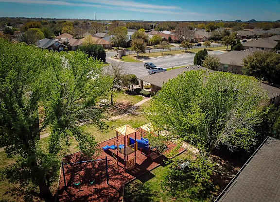 A playground with a swing set and a slide is surrounded by trees.