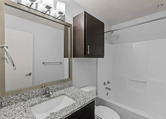 A bathroom with a sink, mirror, toilet and bathtub.
