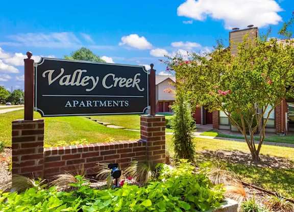 A sign for Valley Creek Apartments is shown in front of a building.