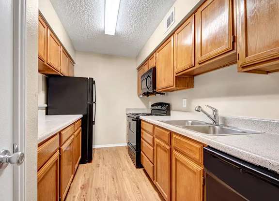 Galley kitchen with wood cabinets and black appliances at South Meadows Apartments, Red Oak, TX