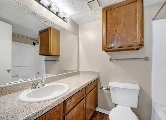Bathroom with wood cabinets and speckled countertop at South Meadows Apartments, Texas, 75154
