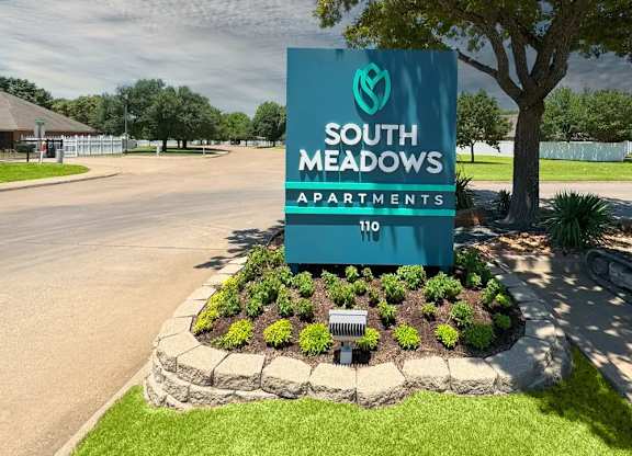 Monument sign with seasonal landscaping and tree shade at South Meadows Apartments, Red Oak, TX