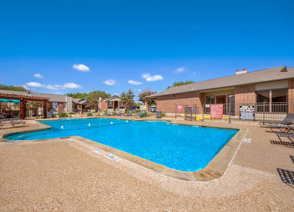 A large outdoor swimming pool surrounded by a sandy area and a few chairs.