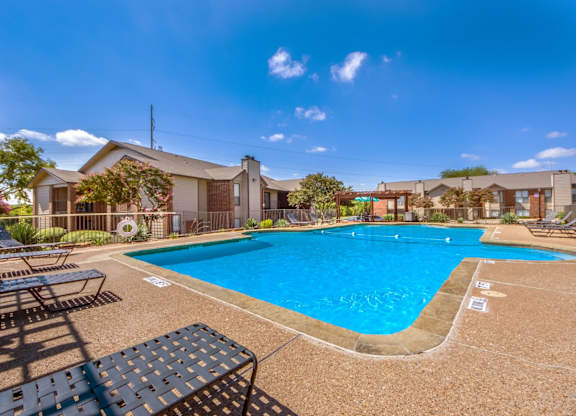 A large outdoor swimming pool surrounded by sun loungers and a building in the background.