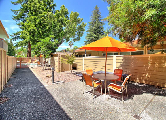 A patio with a table and chairs and an orange umbrella.
