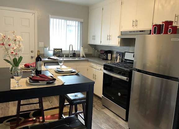 A kitchen with a table set for two with a bottle of wine and a vase of flowers.