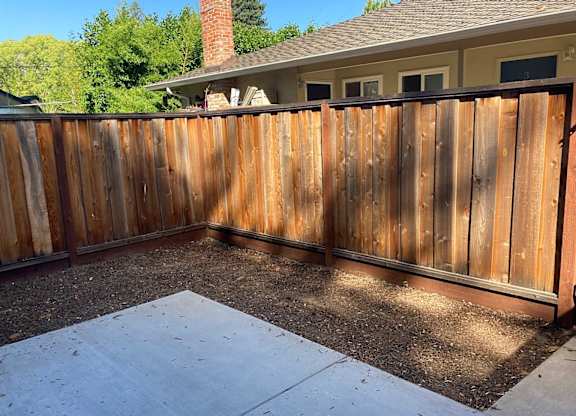 A wooden fence surrounds a concrete patio.