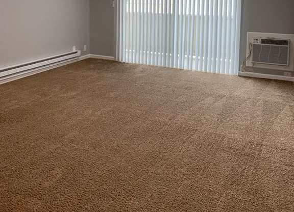 A room with a carpeted floor and a window with blinds.