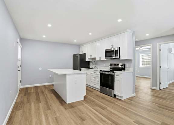 A modern kitchen with white cabinets and a wooden floor.